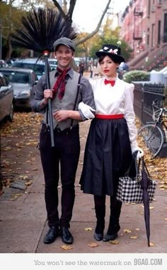 a man and woman dressed in costume standing next to each other on a sidewalk with umbrellas