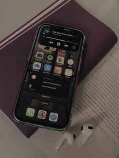 an iphone sitting on top of a book next to earbud headset and headphones