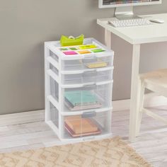 a desk with a computer, keyboard and clear storage bins on the bottom shelf