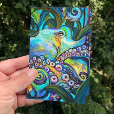 a hand holding up a small card with an octopus on it's face and colorful swirls in the background