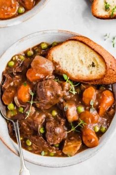 a bowl filled with meat and vegetables next to two slices of bread on top of a table