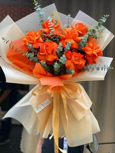 a bouquet of orange flowers is wrapped in white paper and tied with yellow ribbon,