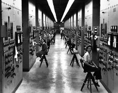 an old black and white photo of people working on electrical equipment in a large room