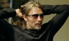 a man with long hair and sunglasses is holding his hands on his head while looking at the mirror