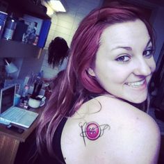 a woman with a tattoo on her shoulder smiling at the camera while standing in front of a laptop computer