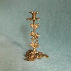 a gold colored candle holder with flowers and leaves on the base, sitting on a blue background