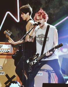 two young men with red hair are playing guitars and singing into microphones on stage