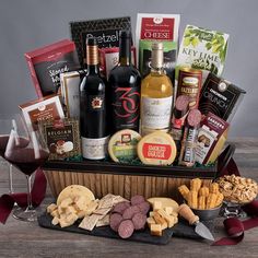 a wine and cheese gift basket with two glasses of red wine, crackers, snacks, and chocolates