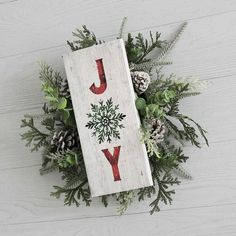 a wooden sign with the word joy on it surrounded by evergreen leaves and pine cones