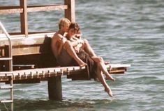 two people are sitting on a dock in the water and one person is holding his head