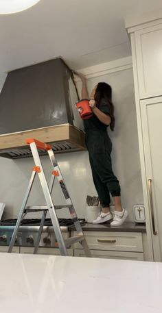 a woman standing on top of a kitchen counter next to a stove and ladders