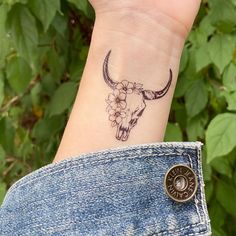 a woman's wrist with a tattoo of a bull skull and flowers on it