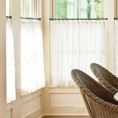 two wicker chairs sitting next to each other in front of a window with white curtains