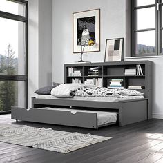 a bed with a book shelf above it in front of two windows and a rug on the floor