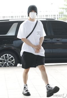 a young man wearing a face mask while walking down the street in front of a car