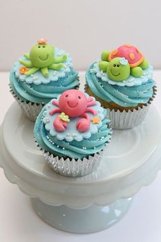 three cupcakes with blue frosting and sea animals on them sitting on a cake plate