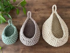 three crocheted baskets sitting on top of a wooden table next to a plant