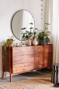 a wooden dresser topped with plants and a round mirror