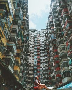 a woman sitting on the ground in front of some tall buildings with balconies