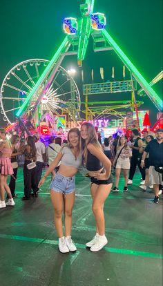 two women standing next to each other in front of a ferris wheel at an amusement park