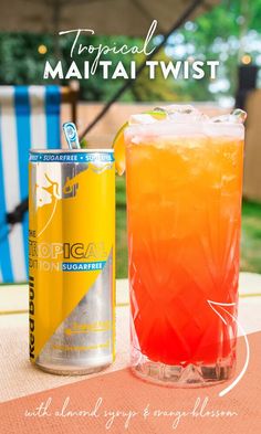 a tall glass filled with orange and red liquid next to a can of tropical mango twist