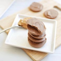 a white plate topped with chocolate covered cookies on top of a wooden cutting board next to a spoon