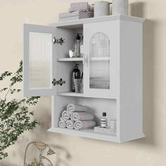 a white bathroom cabinet with towels and other items on it's shelf next to a potted plant