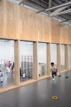 children are playing in an indoor gym with wooden walls and large windows that look out onto the outdoors