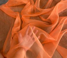 a person's hand on an orange sheer fabric