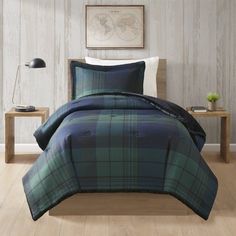 a bed with blue and green plaid comforter in a room next to a table