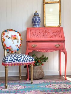 a pink desk and chair with a mirror on it next to a blue floral rug