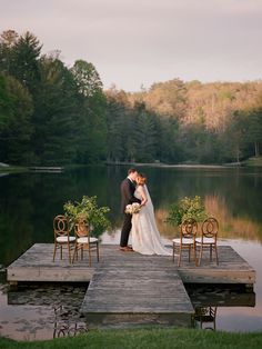 a bride and groom kissing on a dock in front of a lake surrounded by chairs