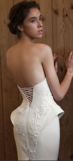 a woman in a white wedding dress leaning against a wooden wall with her hand on the side