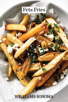 a white bowl filled with french fries covered in feta cheese and parmesan