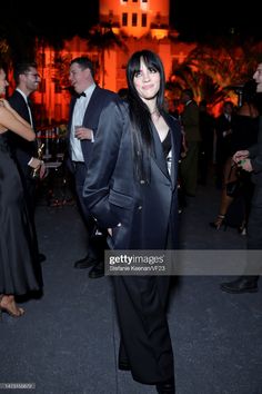 a woman standing in front of a building at night wearing a black suit and tie