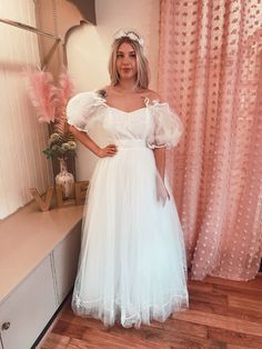 a woman standing in front of a mirror wearing a white dress with puffy sleeves