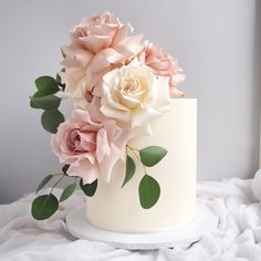 there is a white cake with pink flowers on the top and green leaves around it