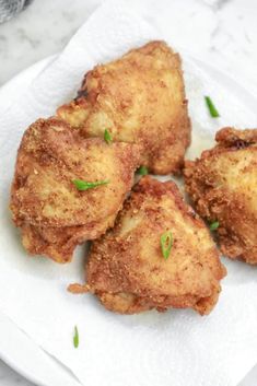 four fried chicken pieces on a white plate with parsley sprinkled around them