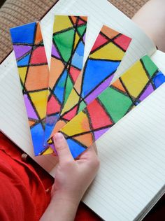 a person holding four pieces of stained glass in front of a notebook with lined pages