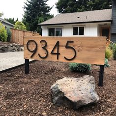 a wooden house number sign sitting in front of a rock