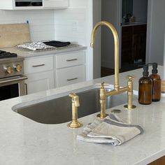 a kitchen with white cabinets and gold faucet, marble counter tops and stainless steel sink