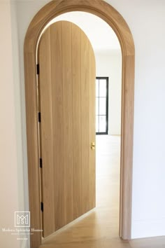 an arched wooden door in the middle of a room with hard wood flooring and white walls