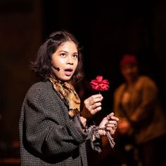 a woman holding a red flower in her right hand while standing next to other people