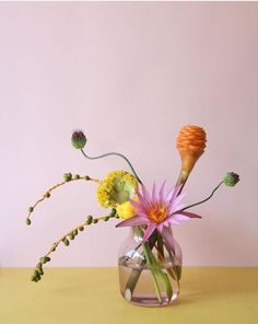 a vase filled with flowers sitting on top of a table next to a pink wall