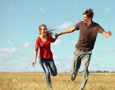 a man and woman running through a field with the sky in the backgroud