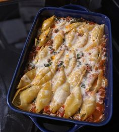 a blue casserole dish filled with pasta and sauce on top of a table