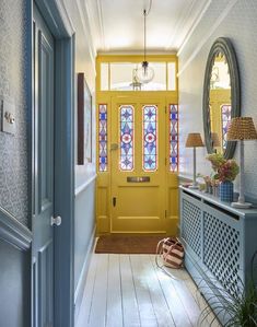 a yellow door is in the hallway next to a blue cabinet and mirror with stained glass windows