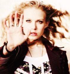 a woman holding her hand up in the air while wearing a black jacket and white t - shirt