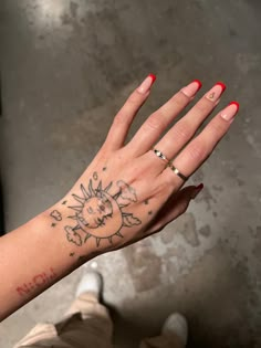 a woman's hand with a sun tattoo on her left wrist and red nail polish