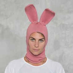 a woman wearing a pink bunny hat and scarf with ears on her head is looking at the camera